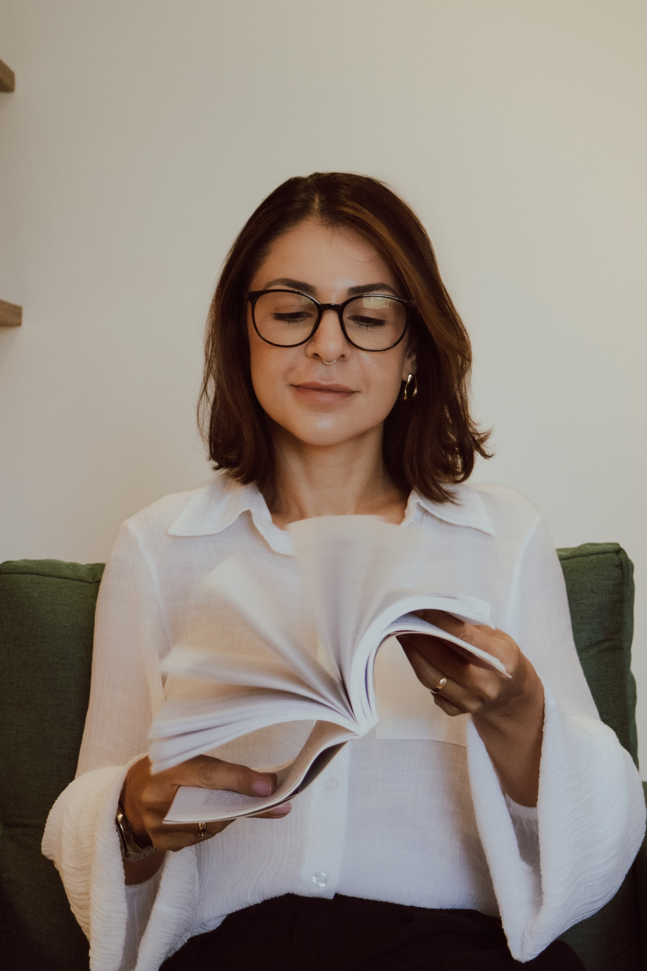 Débora Vieira Carpes folheando um livro sentada em poltrona verde, em seu consultório